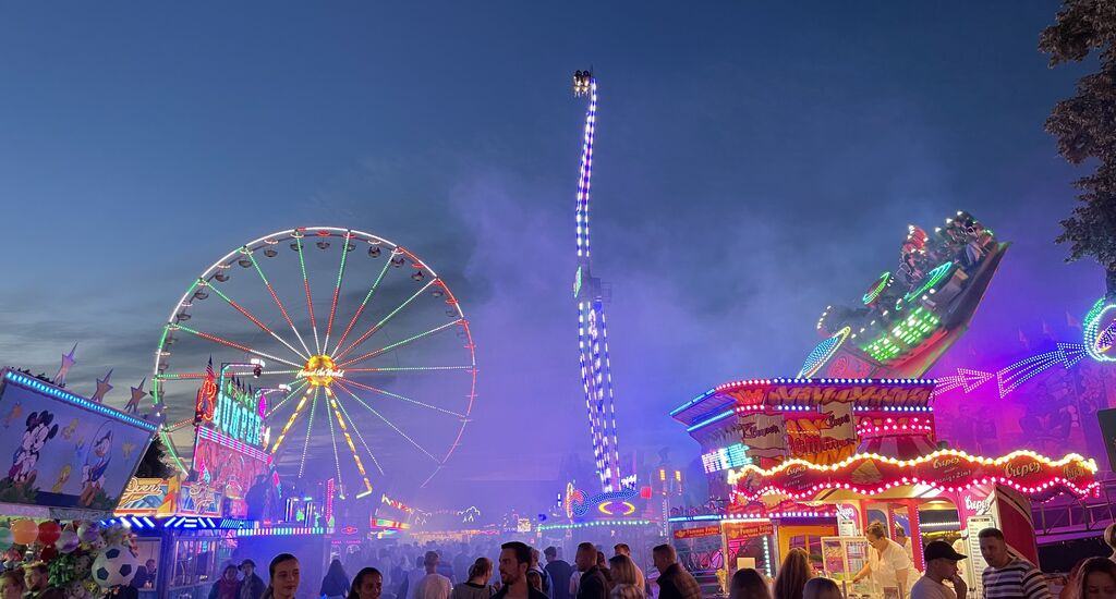 Abends schlendert fröhliche Menschen über den Jahrmarkt, umgeben von Ständen und Fahrgeschäften